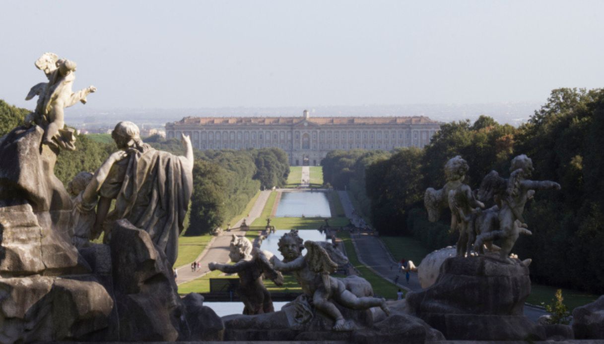 Foto panoramica della Reggia di Caserta e dei suoi giardini, fra i luoghi turistici più visitati ed apprezzati d'Italia, con statue in primo piano