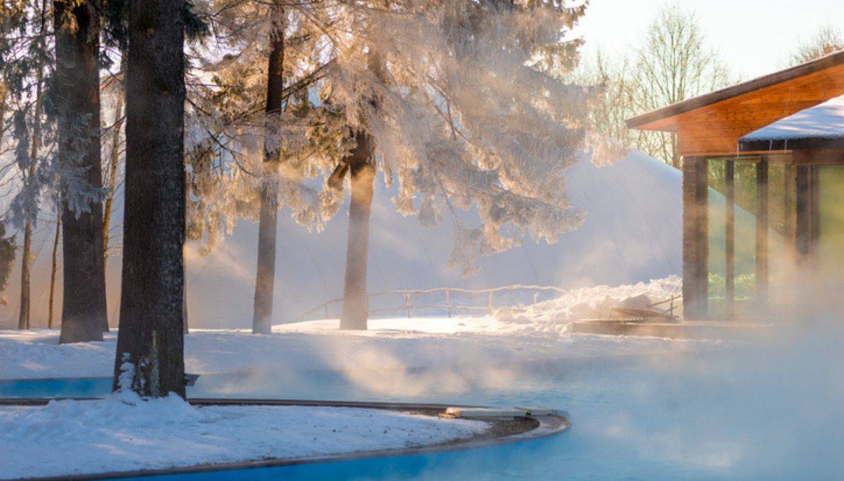 Piscina termale con acqua calda all'aperto immersa in un paesaggio innevato, con vapore che proviene dall'acqua