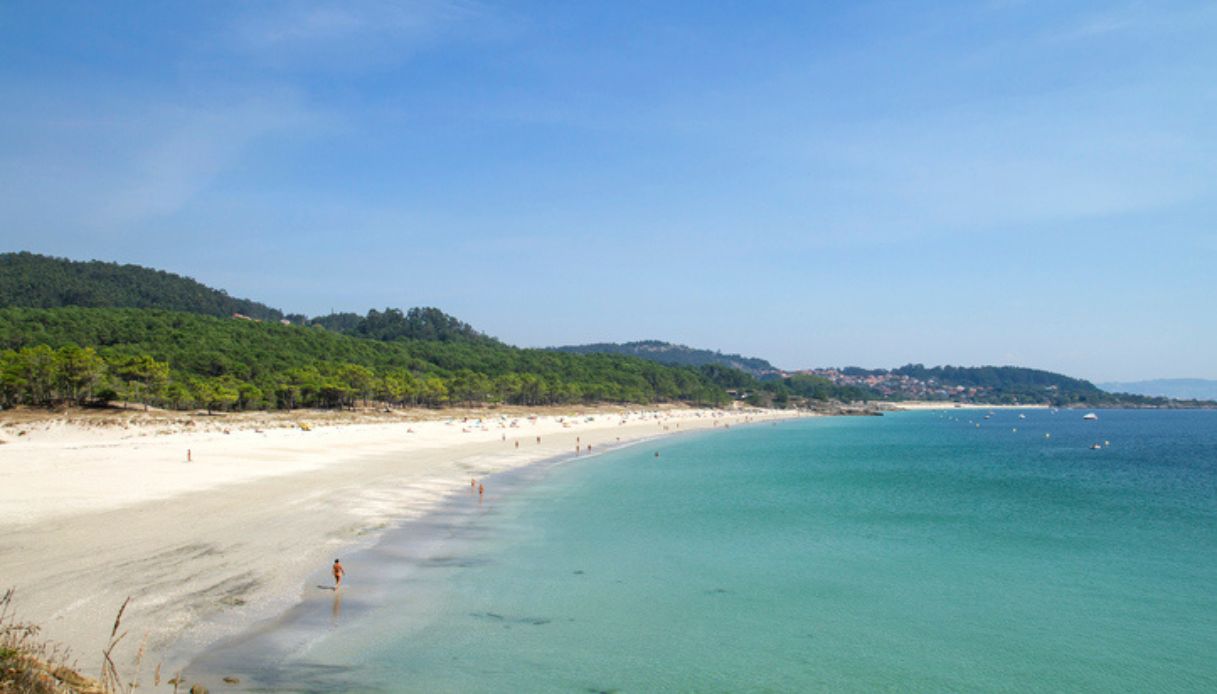 Vista dall'alto di una spiaggia nudista, con sabbia bianca e mare turchese, in mezzo alla natura