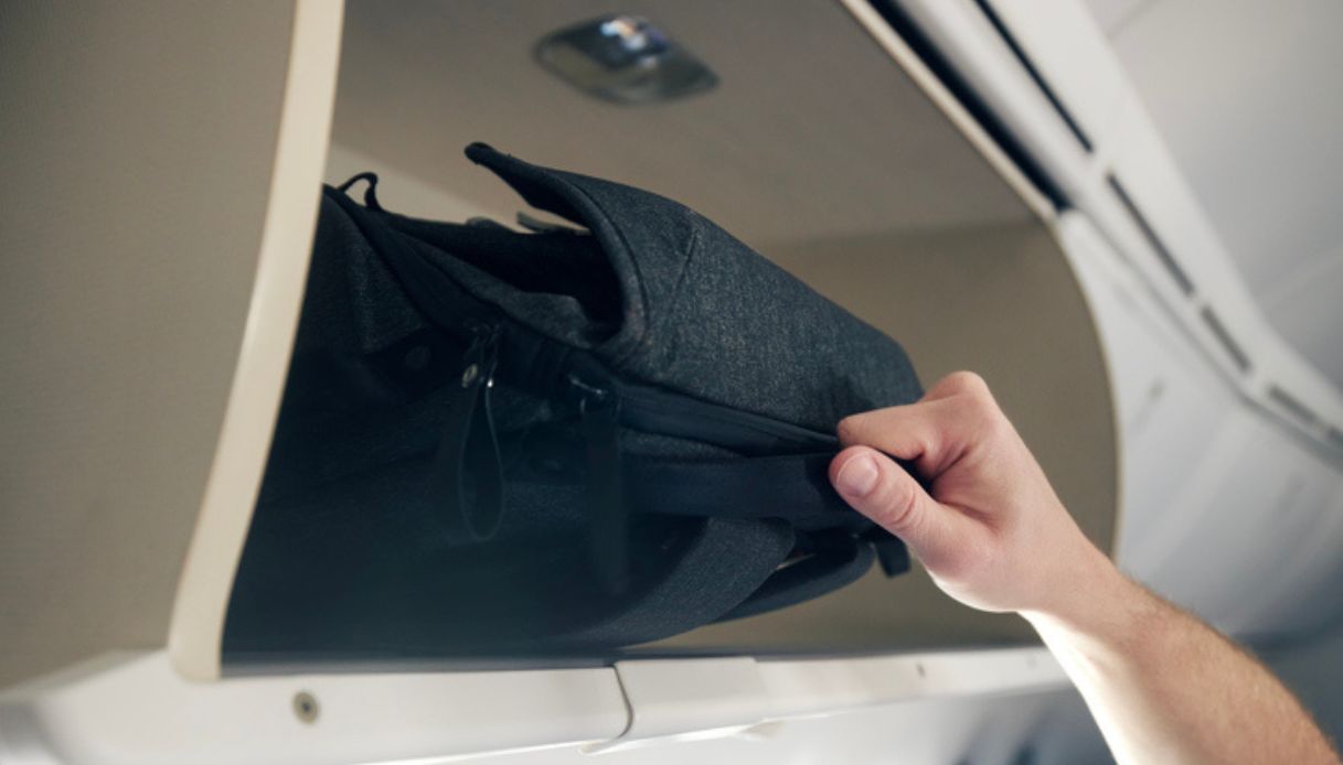 Passeggero tenta di prendere un bagaglio a mano dalla cappelliera in aereo