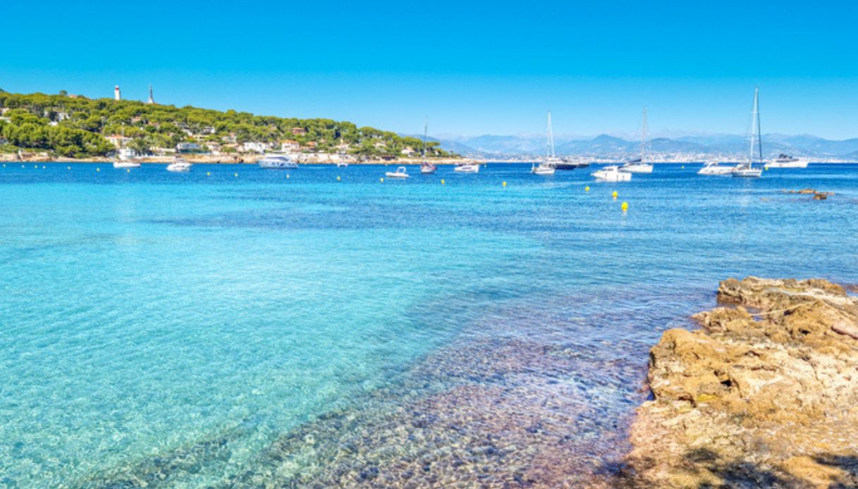 Panorama del mare di capo di Antibes, in Francia, con acqua cristallina in primo piano e barche sullo sfondo