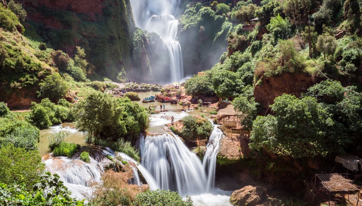 Vista delle cascate di Ouzoud nei pressi di Beni Mellal in Marocco, con una ricca vegetazione e persone che fanno il bagno