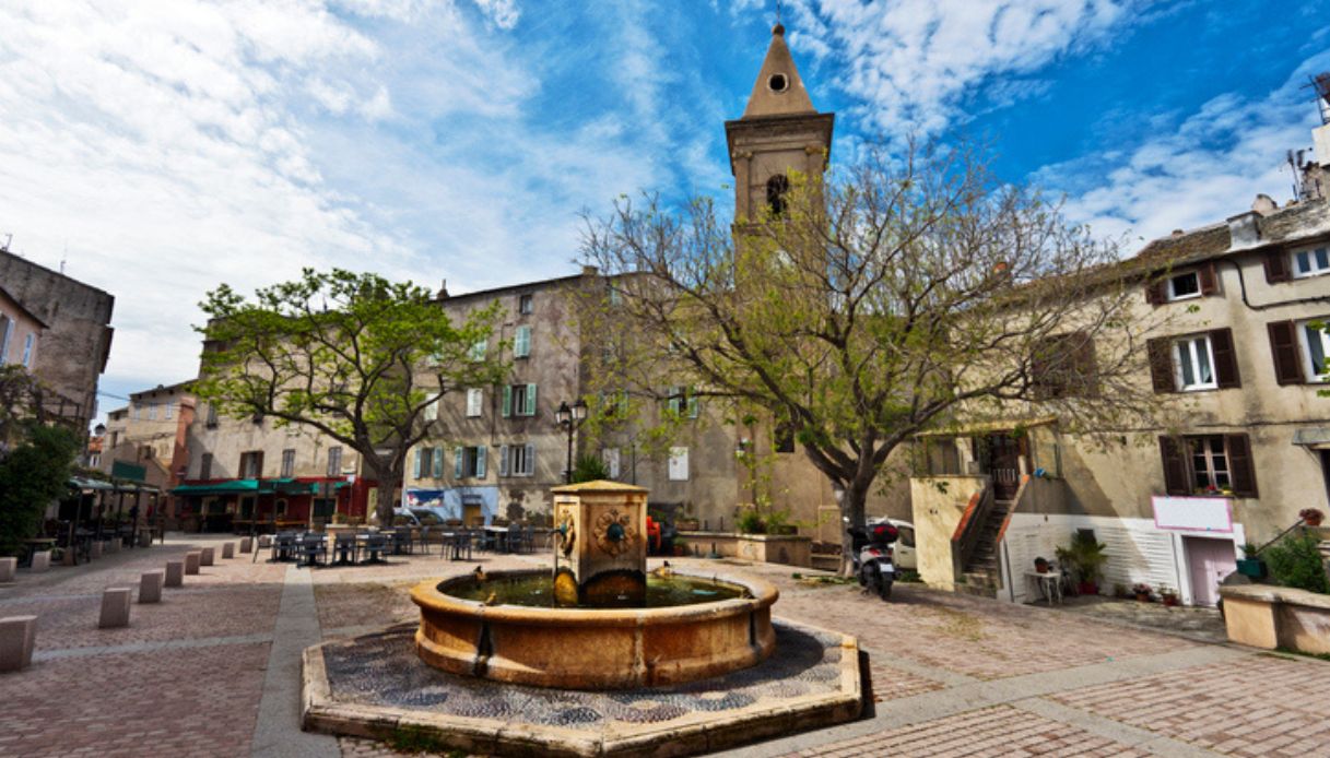 Centro storico del borgo di Saint Florent in Corsica, con fontana in primo piano e campanile sullo sfondo