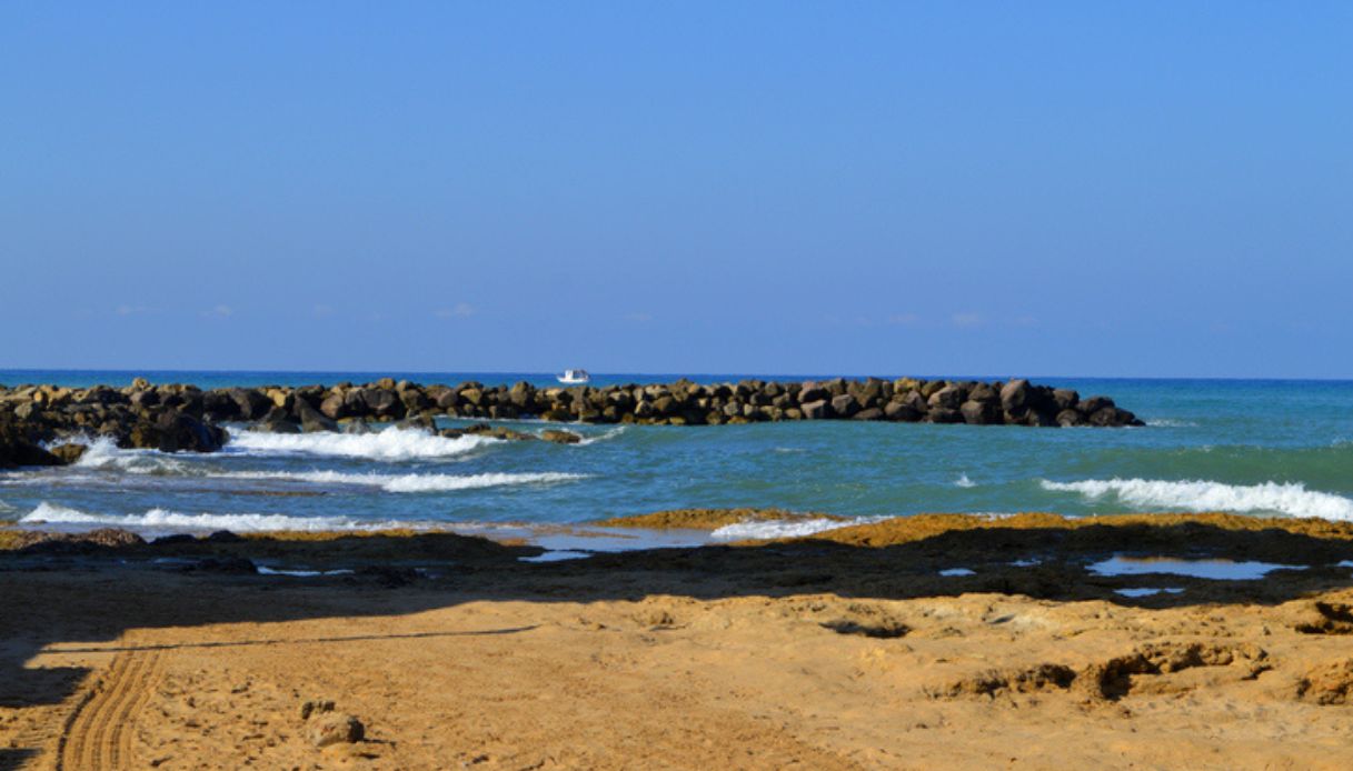 Vista della spiaggia dorata di Punta Secca, in Sicilia, con mare mosso e scogli