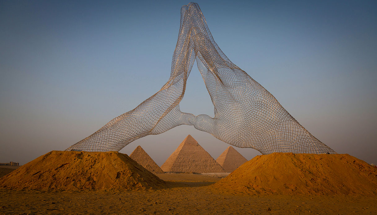 Des mains énormes émergent du désert à l’ombre des pyramides de Gizeh