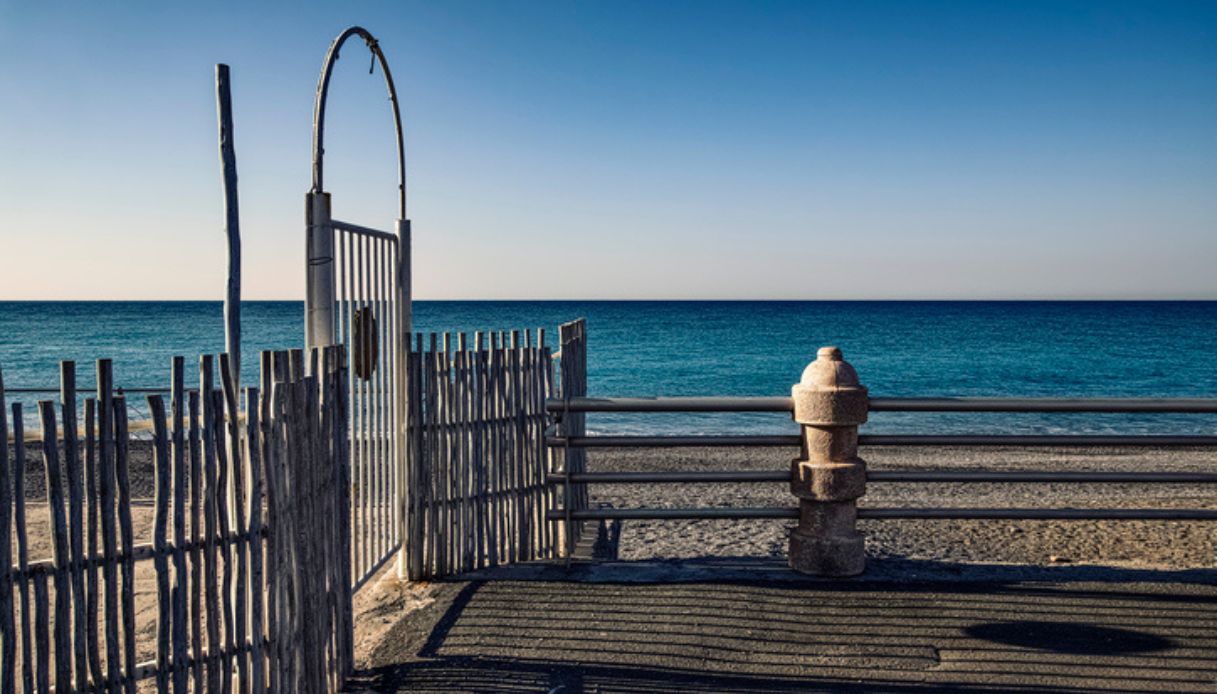 Vista del lungomare di Bordighera, in Liguria, con sabbia chiara ed un cancello chiuso