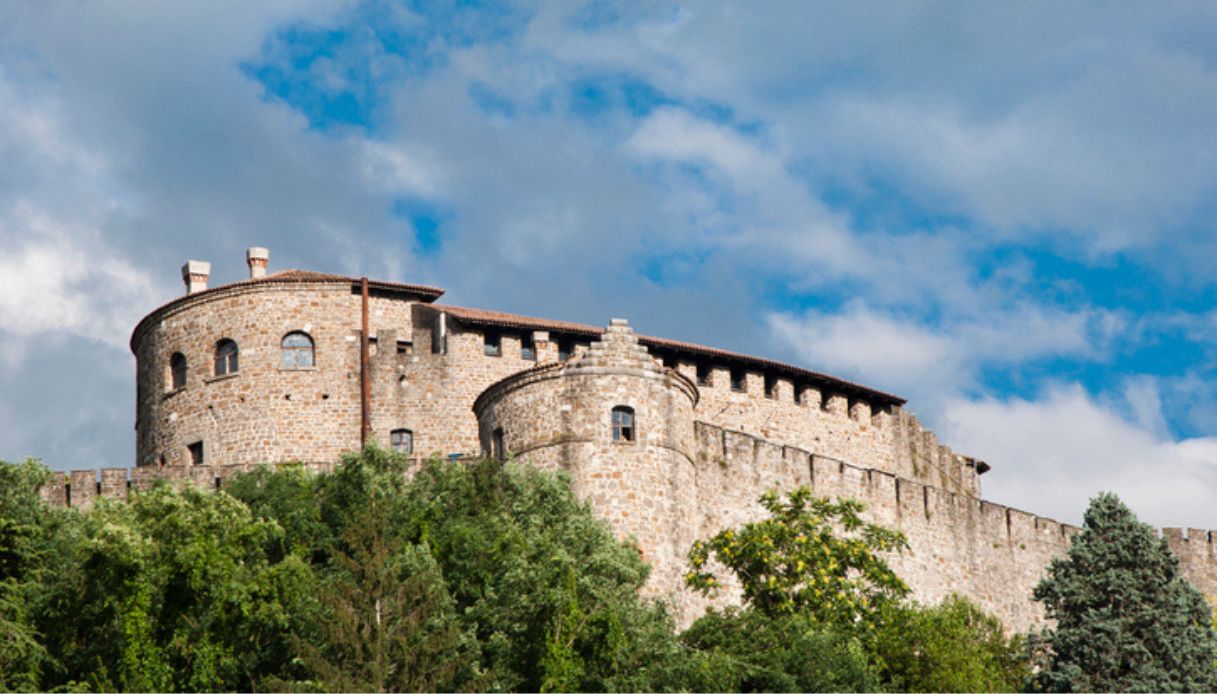 Foto dal basso del Castello di Gorizia, con in primo piano alberi verdi del parco circostante