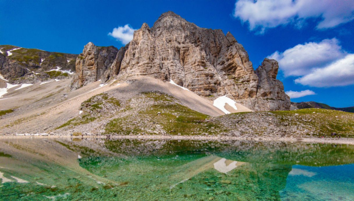 Foto del Lago di Pilato, nelle Marche, con cielo sereno e monte sullo sfondo che si riflette sull'acqua