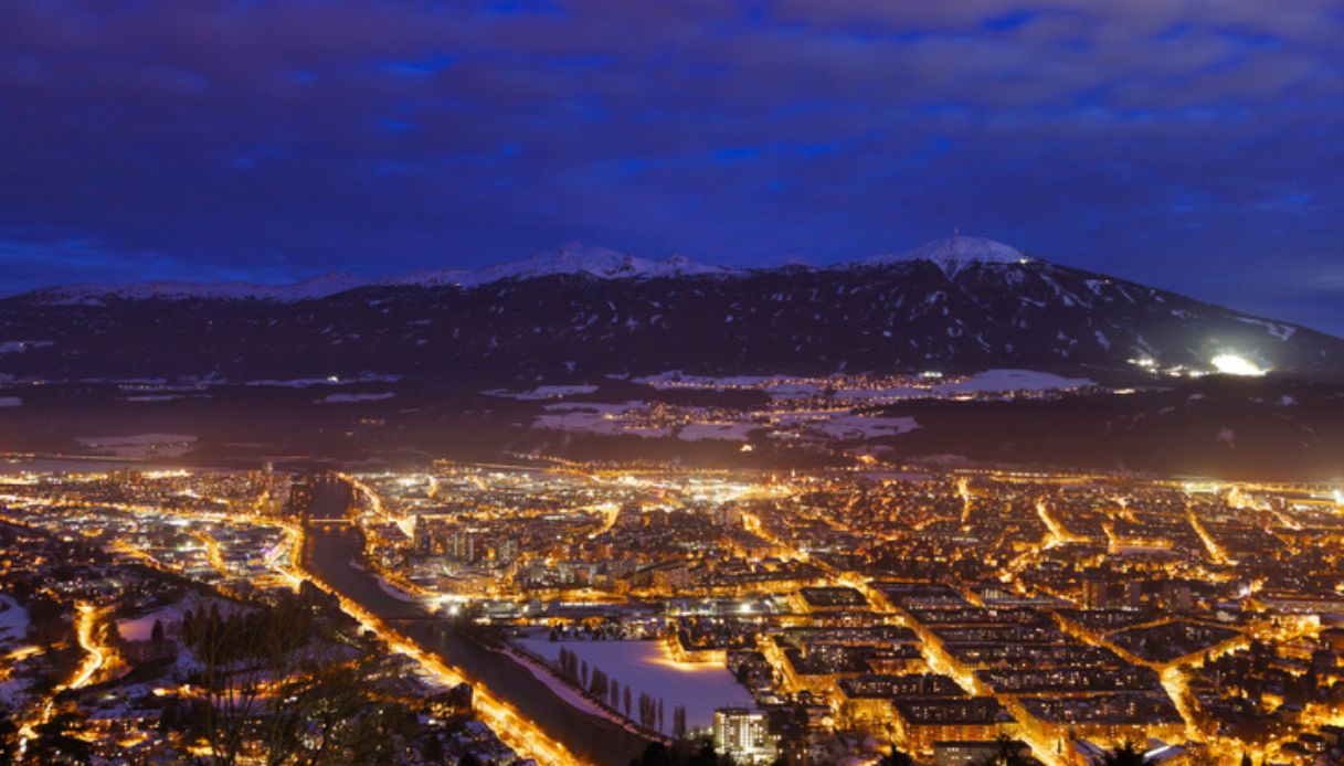 La città di Innsbruck vista dall'alto, con le luci accese e la neve sulle montagne sullo sfondo