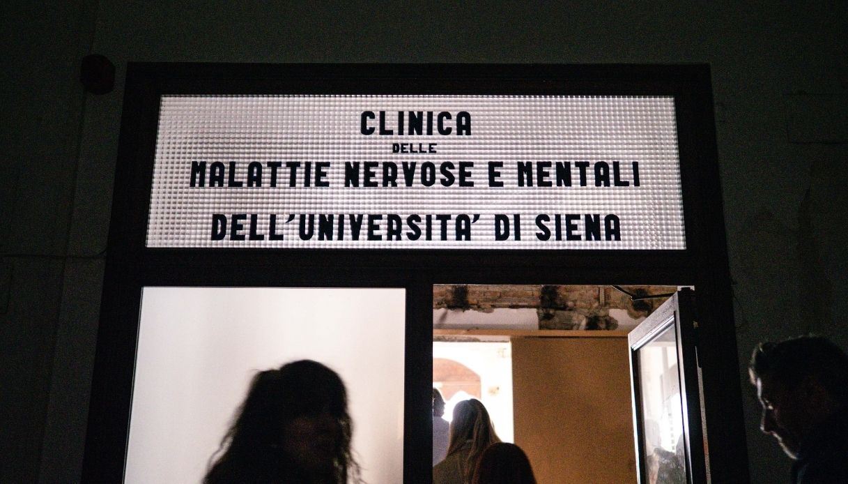 Ingresso illuminato con insegna "Clinica delle Malattie Nervose e Mentali dell'Università di Siena" al Santa Maria della Scala