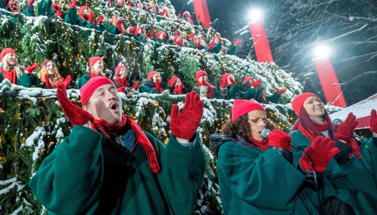Coristi con cappelli, sciarpe e guanti rossi e mantelle verdi cantano sui livelli di un grande albero di Natale nella Foresta Nera